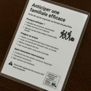 Photographie d’une fiche de survie plastifiée en français sur table en bois, illustrant un plan d’évacuation familiale stratégique sans afficher le contenu de façon lisible